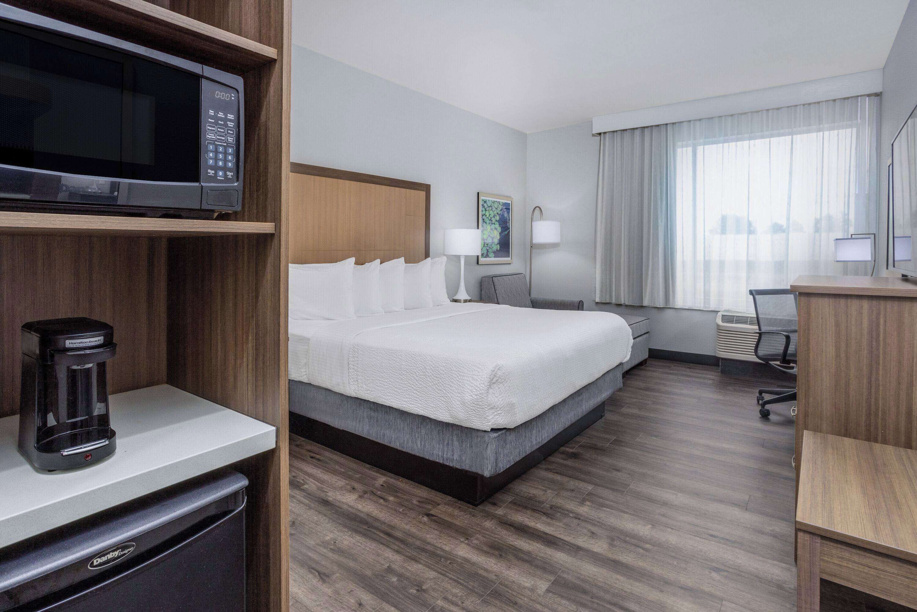 Una camera d'hotel con un letto, un forno a microonde, una macchina del caffè, una scrivania e una sedia.