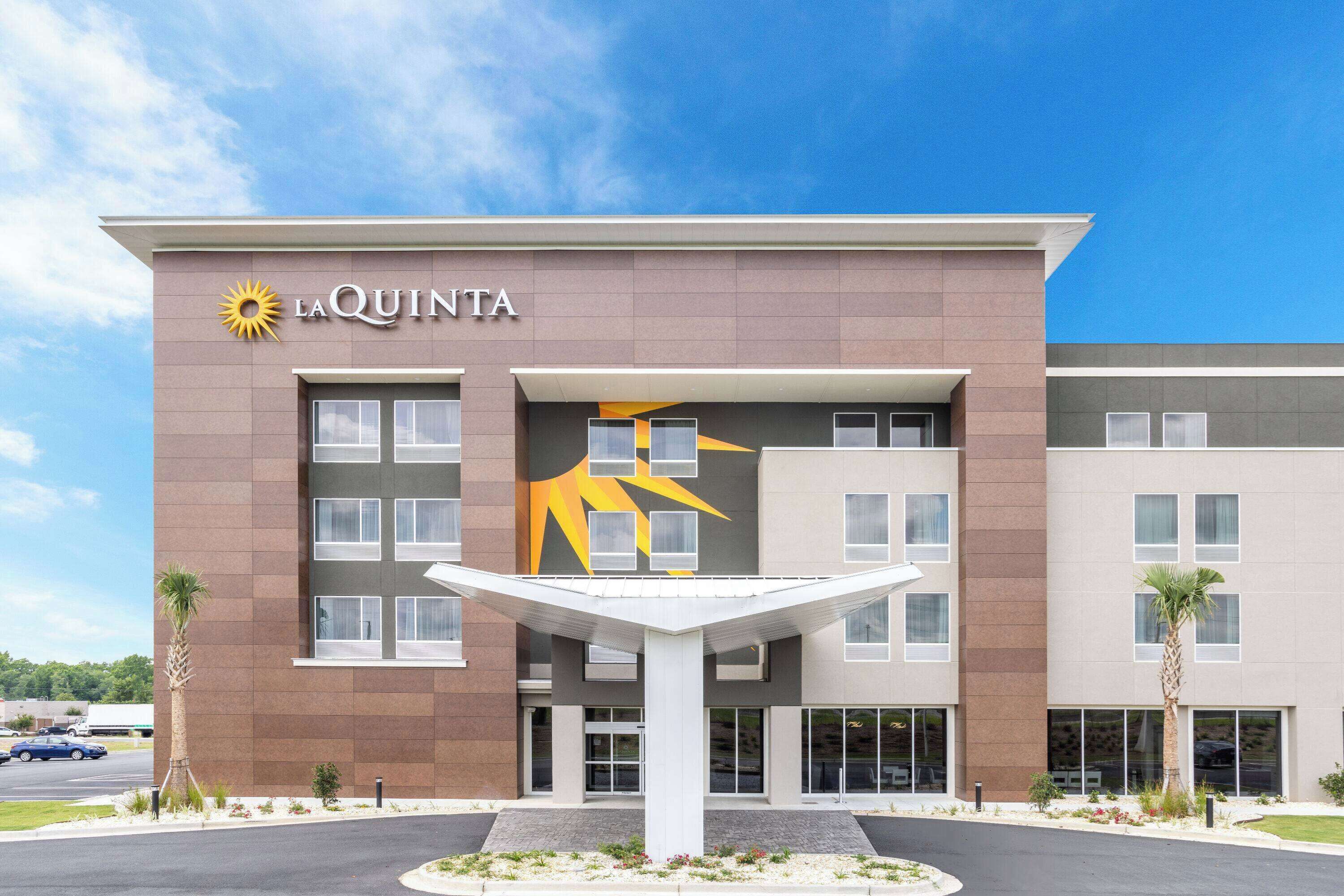 A modern hotel with a prominent sun logo, a central courtyard, and a parking lot.