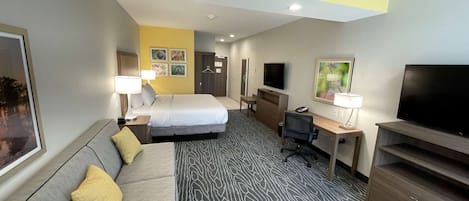 A hotel room with a bed, a sofa, a desk, a TV, and a desk lamp.