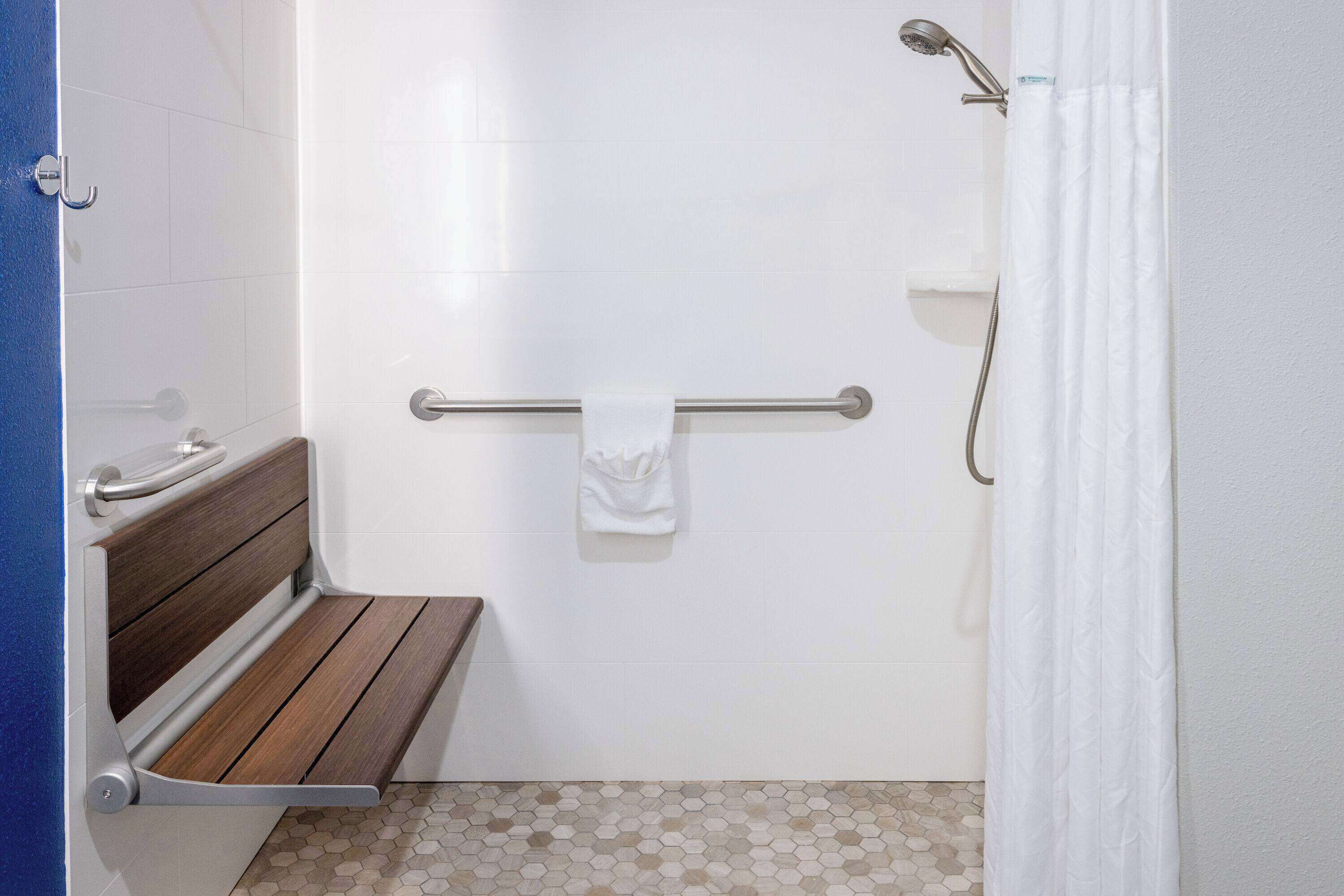 Un baño con banca de madera, barra de apoyo y ducha con cortina.