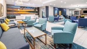 A modern hotel lobby with a large mural, seating area, and a reception desk. - La Quinta Inn & Suites by Wyndham Valdosta (Valdosta)