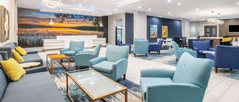 A modern hotel lobby with a large mural, seating area, and a reception desk.
