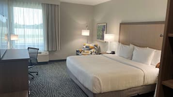 A hotel room with a large bed, a desk, a chair, a lamp, and a painting on the wall.