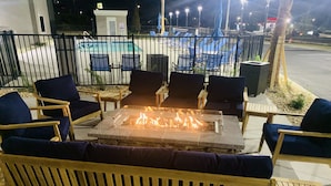 An outdoor seating area with a fire pit, lounge chairs, and a pool in the background. - La Quinta Inn & Suites by Wyndham Valdosta (Valdosta)