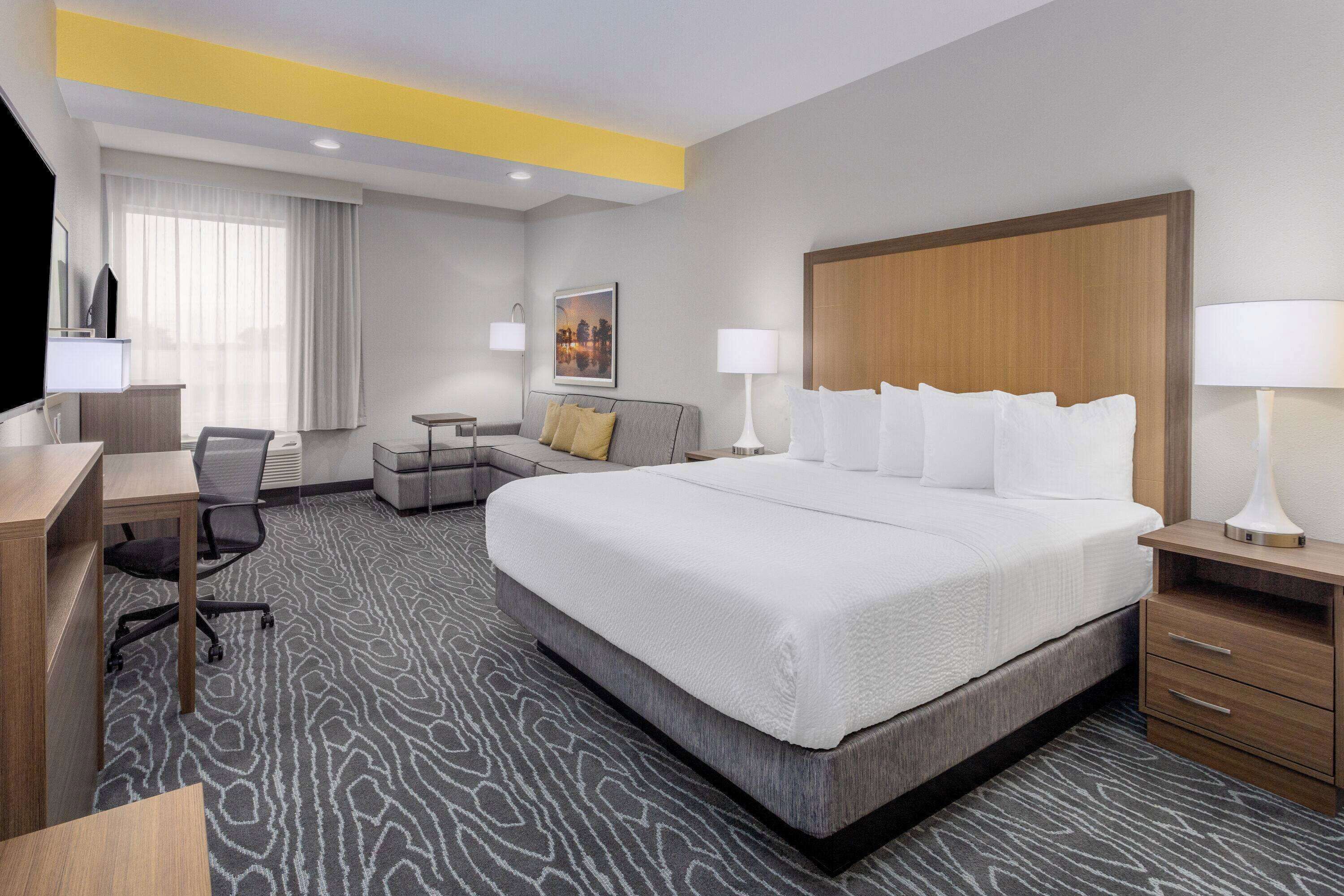 A hotel room with a large bed, a desk, a chair, a small table, and a TV.