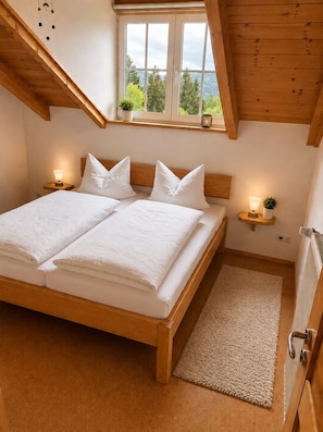 A bedroom with a wooden bed, two bedside tables with lamps, a window with a view, and a radiator.