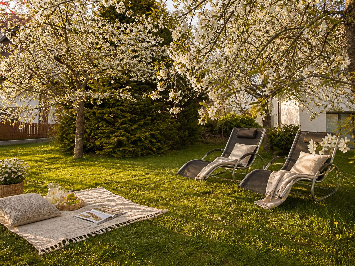 A garden with two lounge chairs, a picnic setup, and blooming trees.