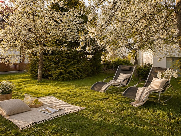 A garden with two lounge chairs, a picnic setup, and blooming trees.
