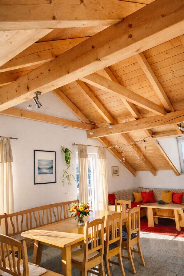 Ein Essbereich mit Holzmöbeln, einer Decke mit freiliegenden Balken und Blick auf ein Wohnzimmer mit einer Couch und Kissen.