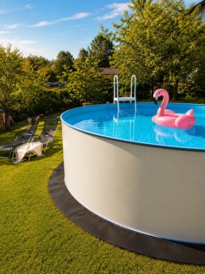 Ein oberirdischer Swimmingpool mit einer Leiter, einem Flamingo-Schwimmspielzeug und Liegestühlen auf einer Rasenfläche.