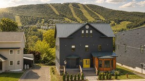 Una moderna casa a due piani con facciata scura, un portico e una piccola struttura in legno simile a una baita.
