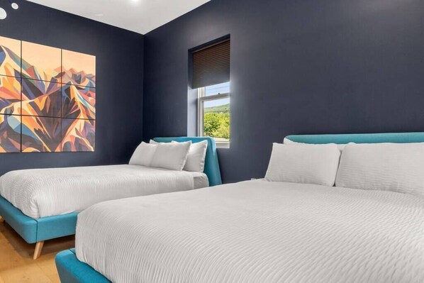 A modern hotel room with two beds, a large abstract painting on the wall, and a window with blinds.