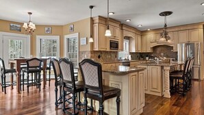 A spacious kitchen with wooden cabinets, a central island, and bar stools. - Luxury 5-BR Mountain Estate 5-Min to Okemo (Ludlow)