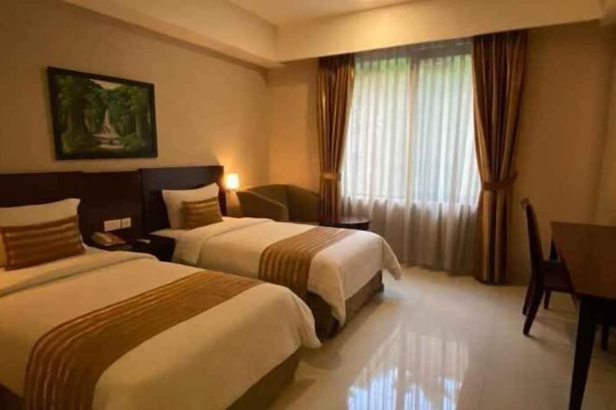 A hotel room with two beds, a desk, a chair, and a painting on the wall.