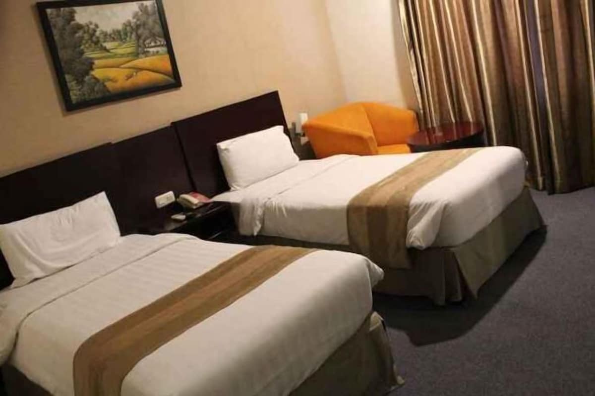 A hotel room with two beds, a nightstand, a lamp, and a painting on the wall.