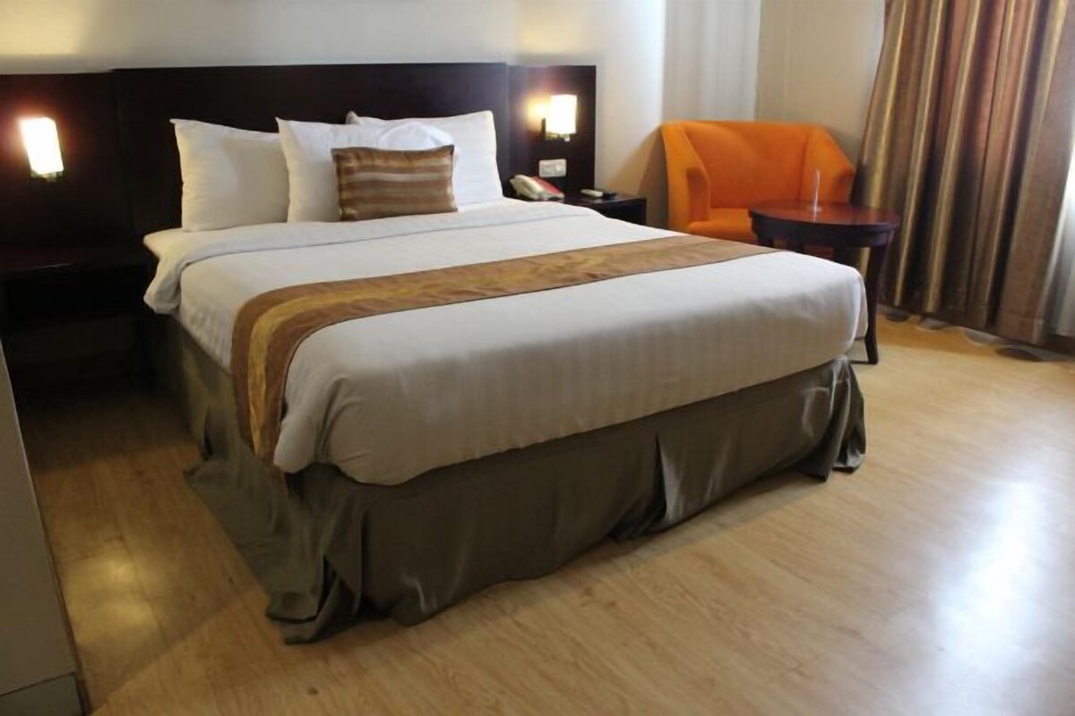 Habitación de hotel con una cama grande, una mesita de noche, un sillón naranja y suelo de madera.