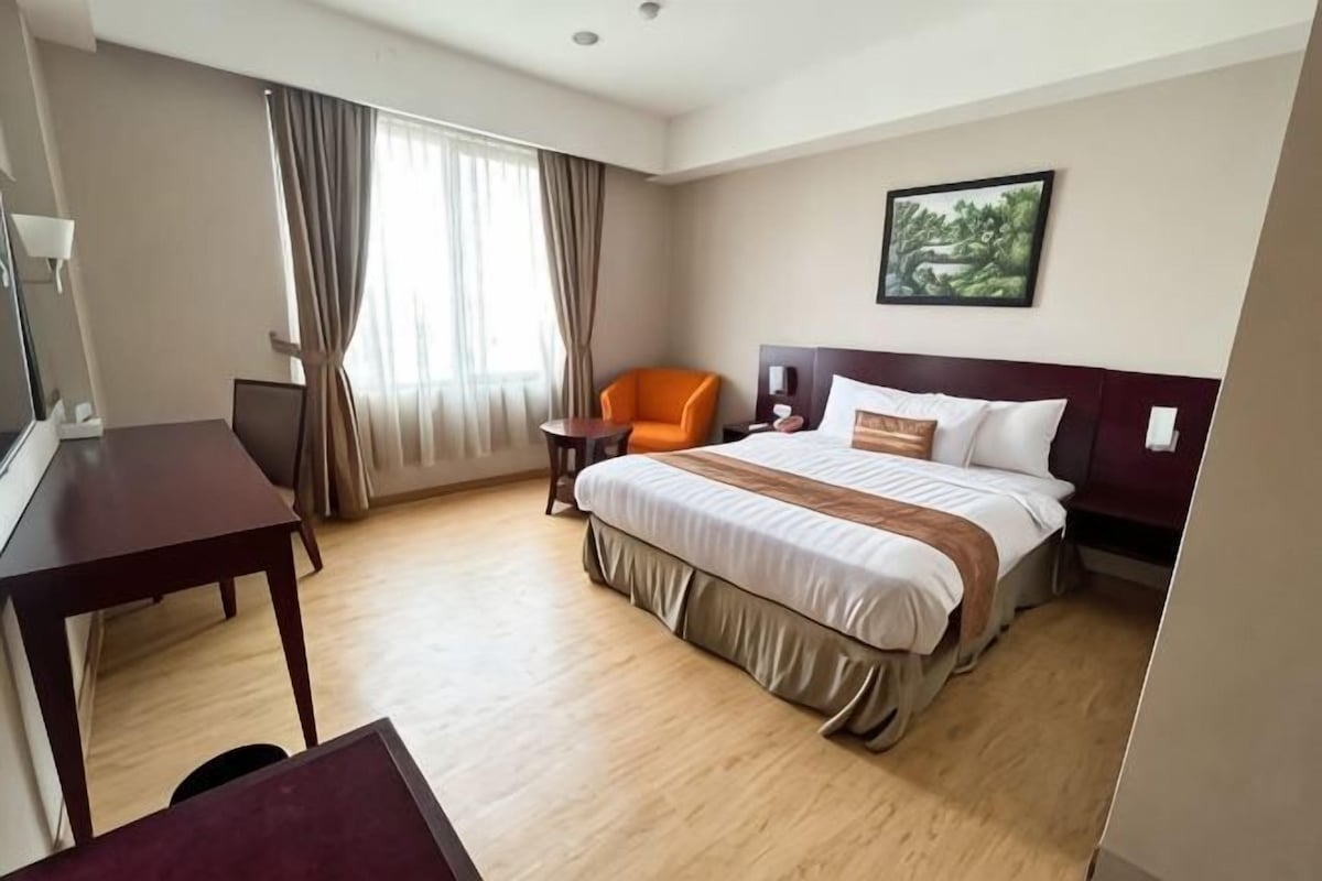 A hotel room with a bed, a desk, a chair, a TV, and a window with curtains.