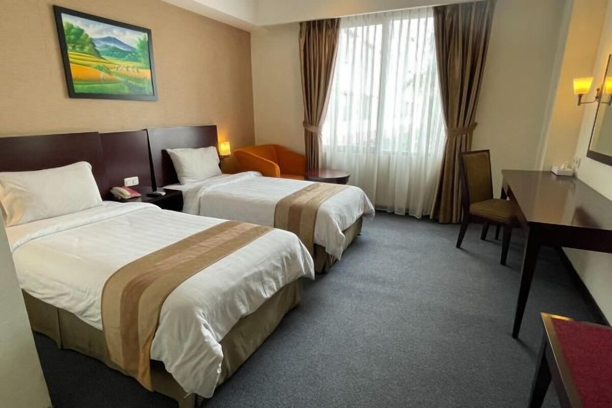 Una habitación de hotel con dos camas, un escritorio, una silla y un cuadro en la pared.