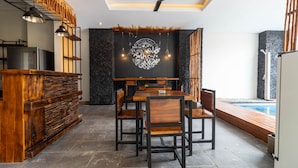 Un comedor moderno con barra de madera, paredes de piedra y color negro, y vista a la piscina.