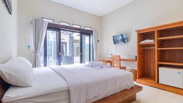 A bedroom with a bed, a wooden wardrobe, a television, and a window with curtains.