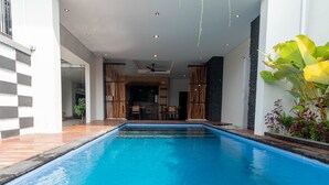 Una piscina con cubierta de madera, un ventilador de techo y vista al espacio interior.