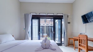 Habitación de hotel con cama, una silla de madera, televisión y vistas a través de un ventanal.