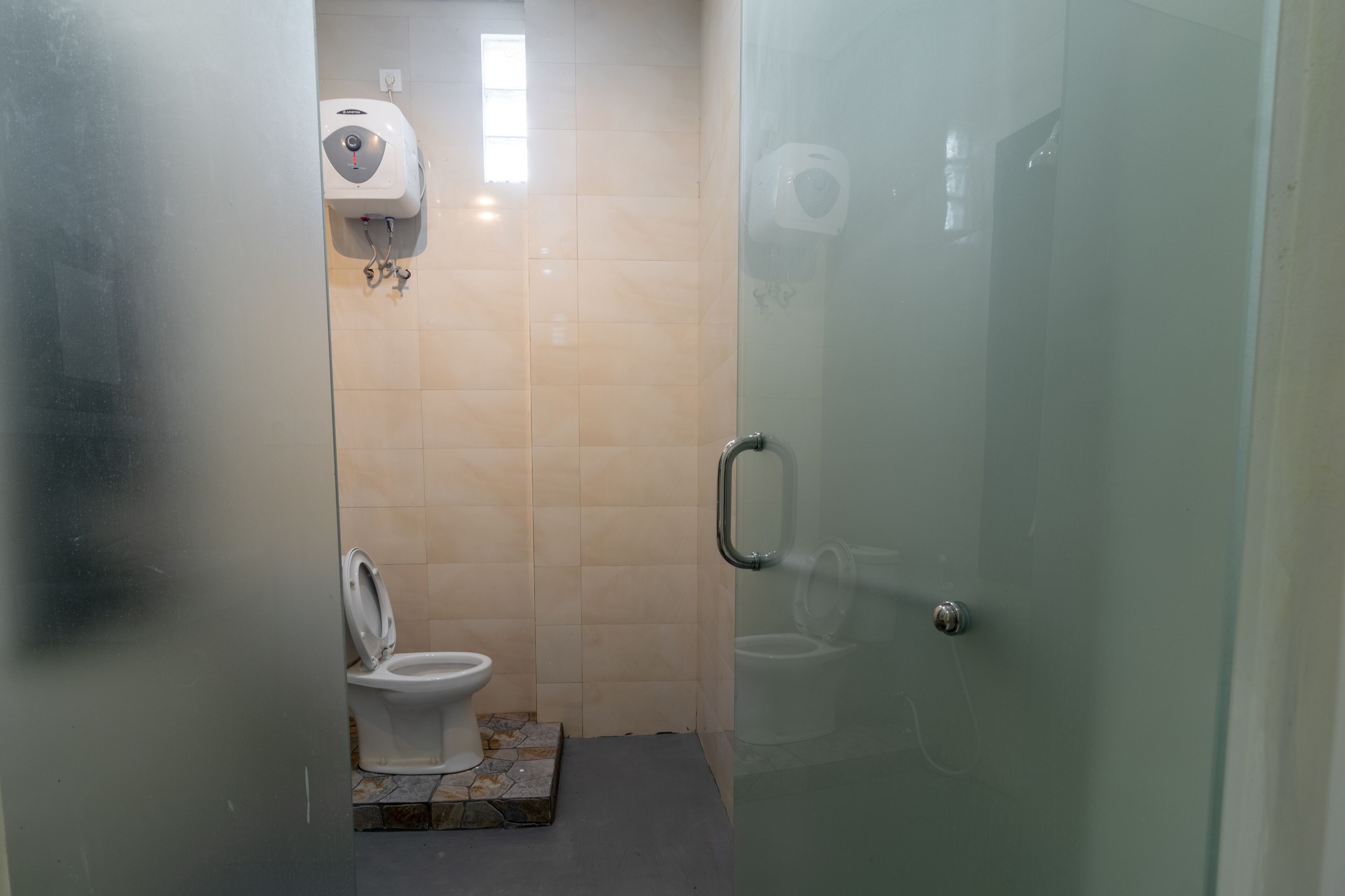 A small bathroom with a toilet, a hand dryer, and a glass shower enclosure.