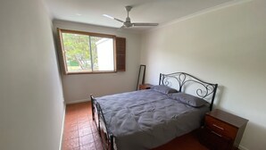 A bedroom with a bed, a nightstand, a ceiling fan, and a window with blinds.
