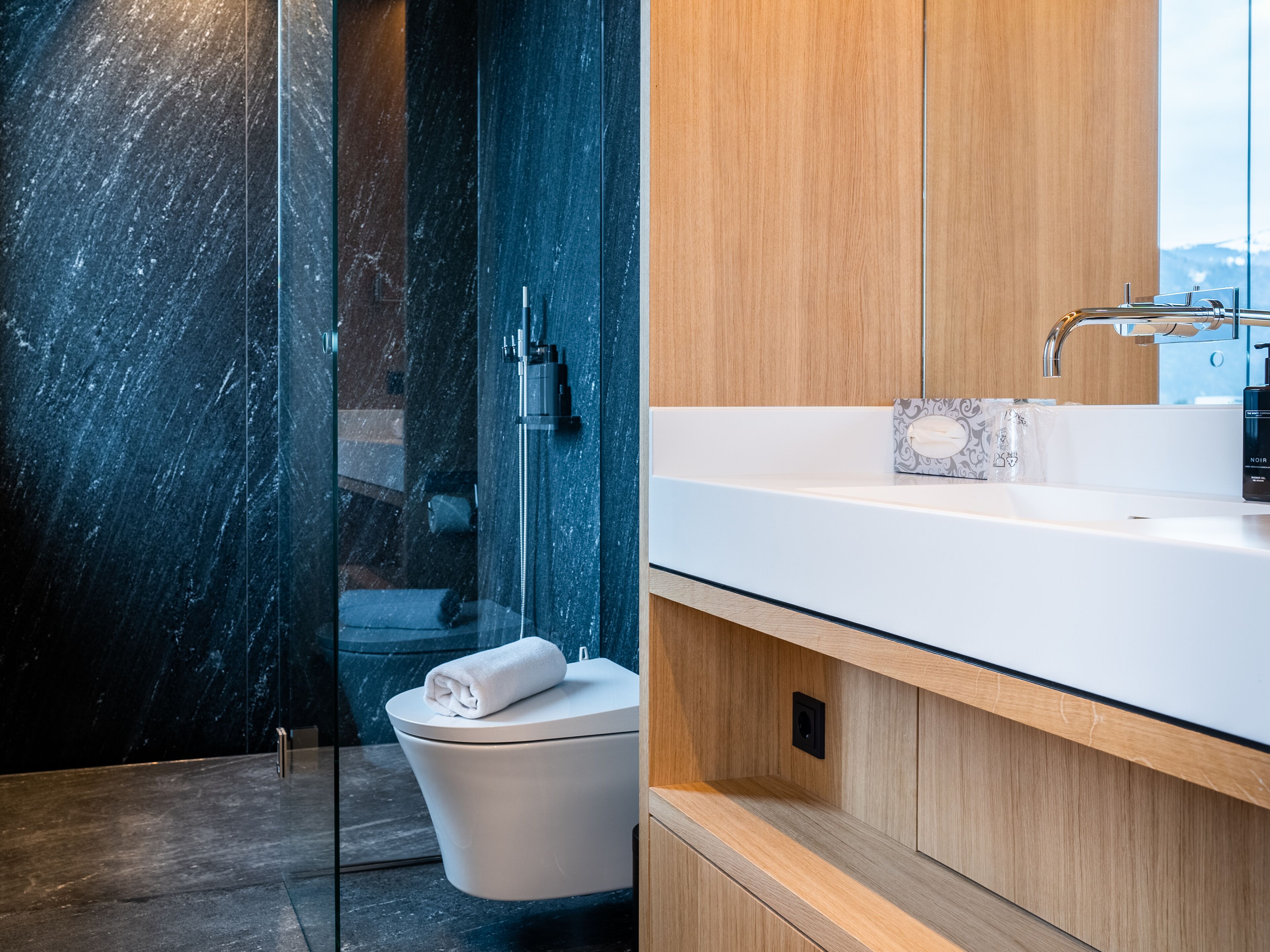 Een moderne badkamer met een douche van marmer, een wit toilet en een houten wastafelmeubel met een wastafel.