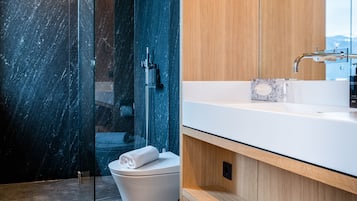Een moderne badkamer met een douche van marmer, een wit toilet en een houten wastafelmeubel met een wastafel.