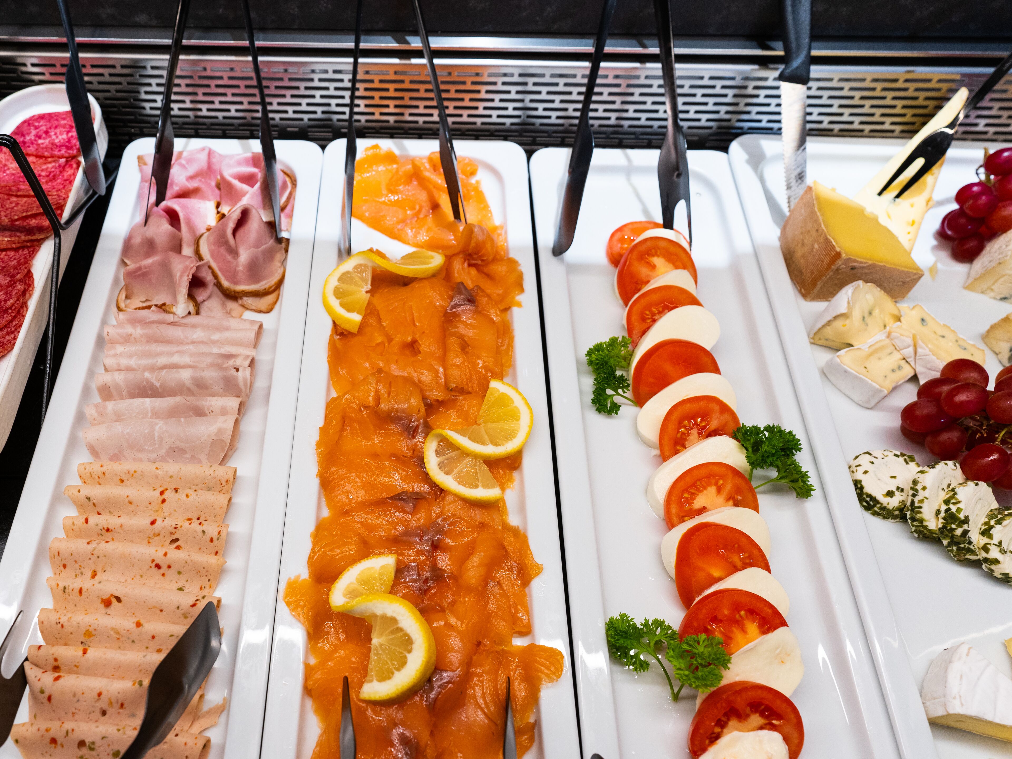 Un bufé con diversos alimentos, incluyendo carnes cortadas, salmón ahumado, tomates, queso y uvas.