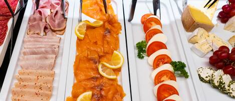 Un bufé con diversos alimentos, incluyendo carnes cortadas, salmón ahumado, tomates, queso y uvas.