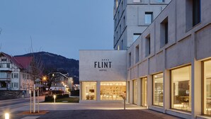 Un hôtel moderne à la façade sobre, doté de grandes fenêtres et d’une enseigne indiquant « FLINT HOTEL ».