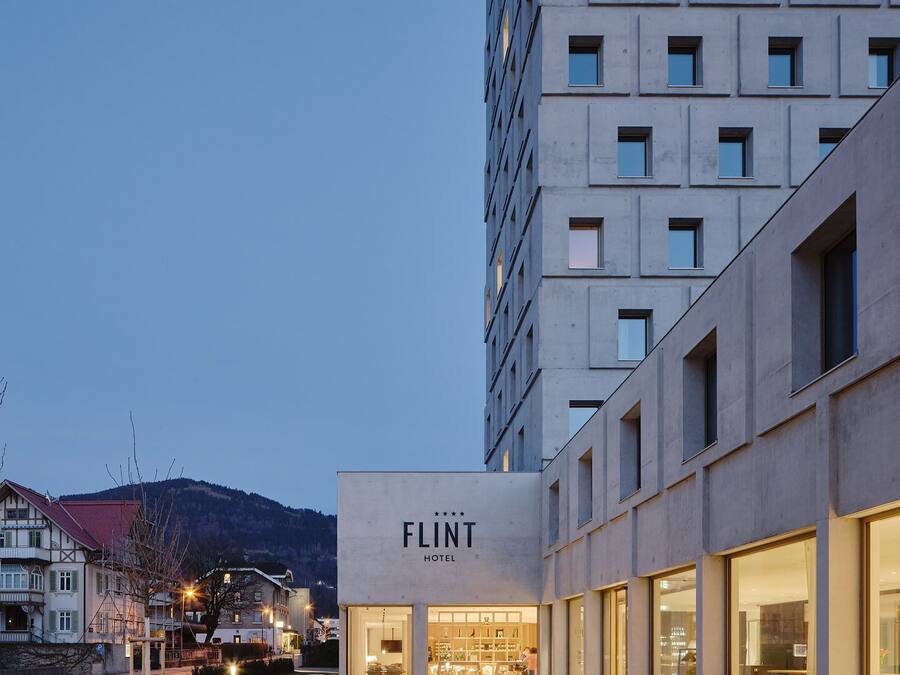 Et moderne hotel med en flad facade, store vinduer og et skilt med teksten "FLINT HOTEL".