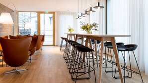 Un espace repas moderne avec une longue table en bois, des tabourets de bar noirs et des chaises orange.