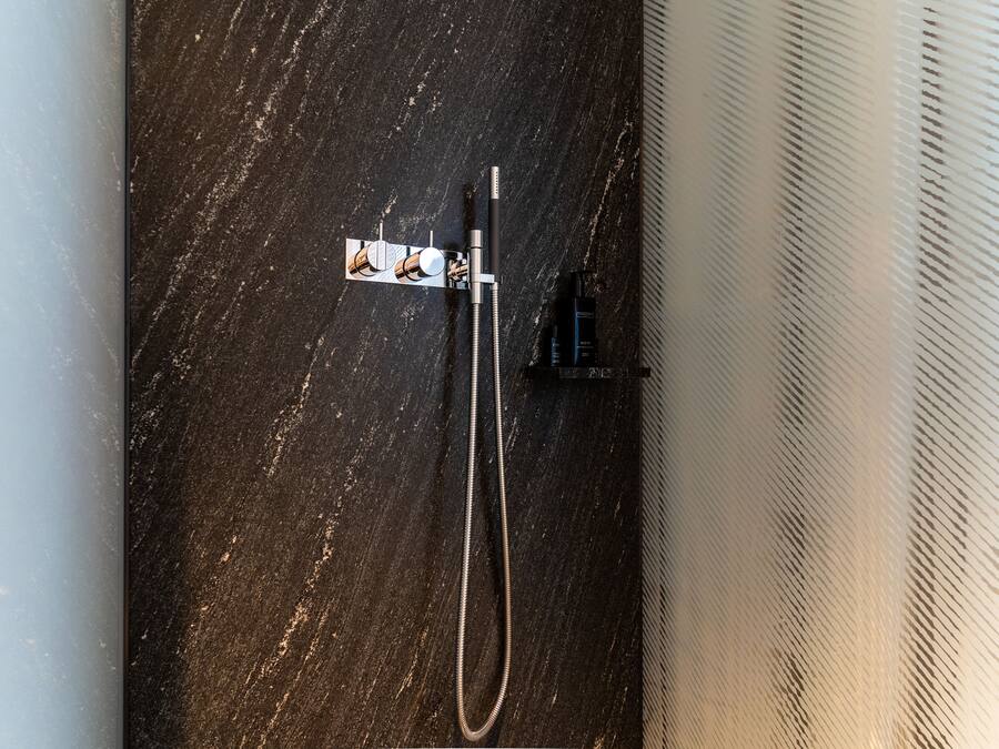 A shower with a handheld attachment and a wall-mounted control panel.