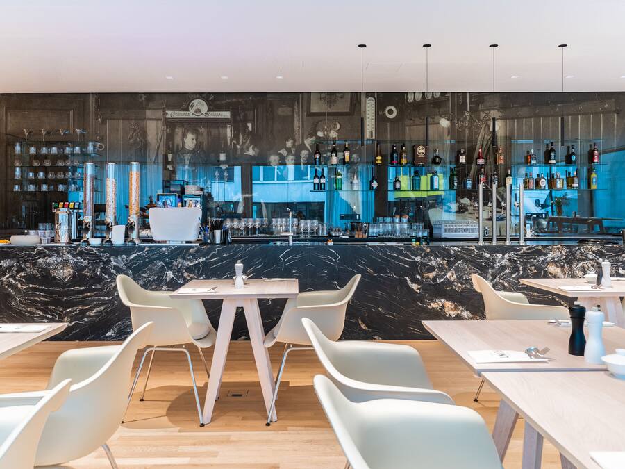 Un bar moderne avec des comptoirs en marbre, des chaises blanches et une variété de bouteilles et de verres.
