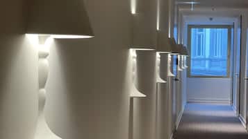 Un pasillo con lámparas modernas empotradas en la pared y piso alfombrado, que conduce a una puerta con vista a un edificio.
