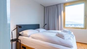A modern hotel room with a large bed, a bedside table with a lamp, and a window with a city view.