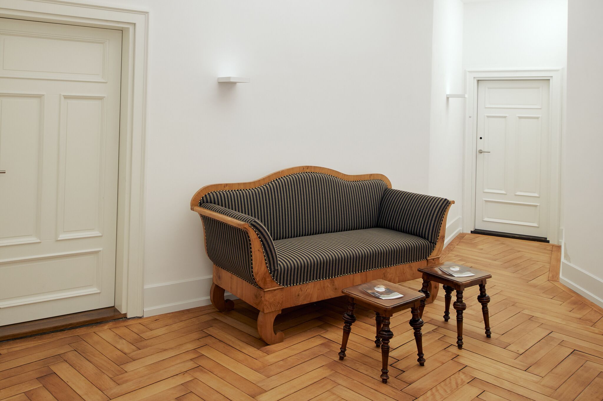 A room with a wooden sofa, two small tables, and white doors.