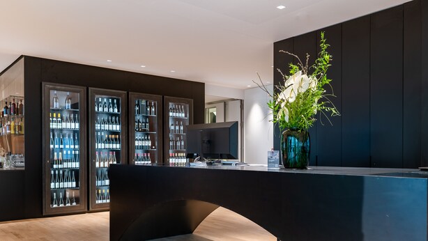Un espace bar moderne avec un comptoir incurvé, un grand écran et, au fond, un assortiment de boissons en bouteille.
