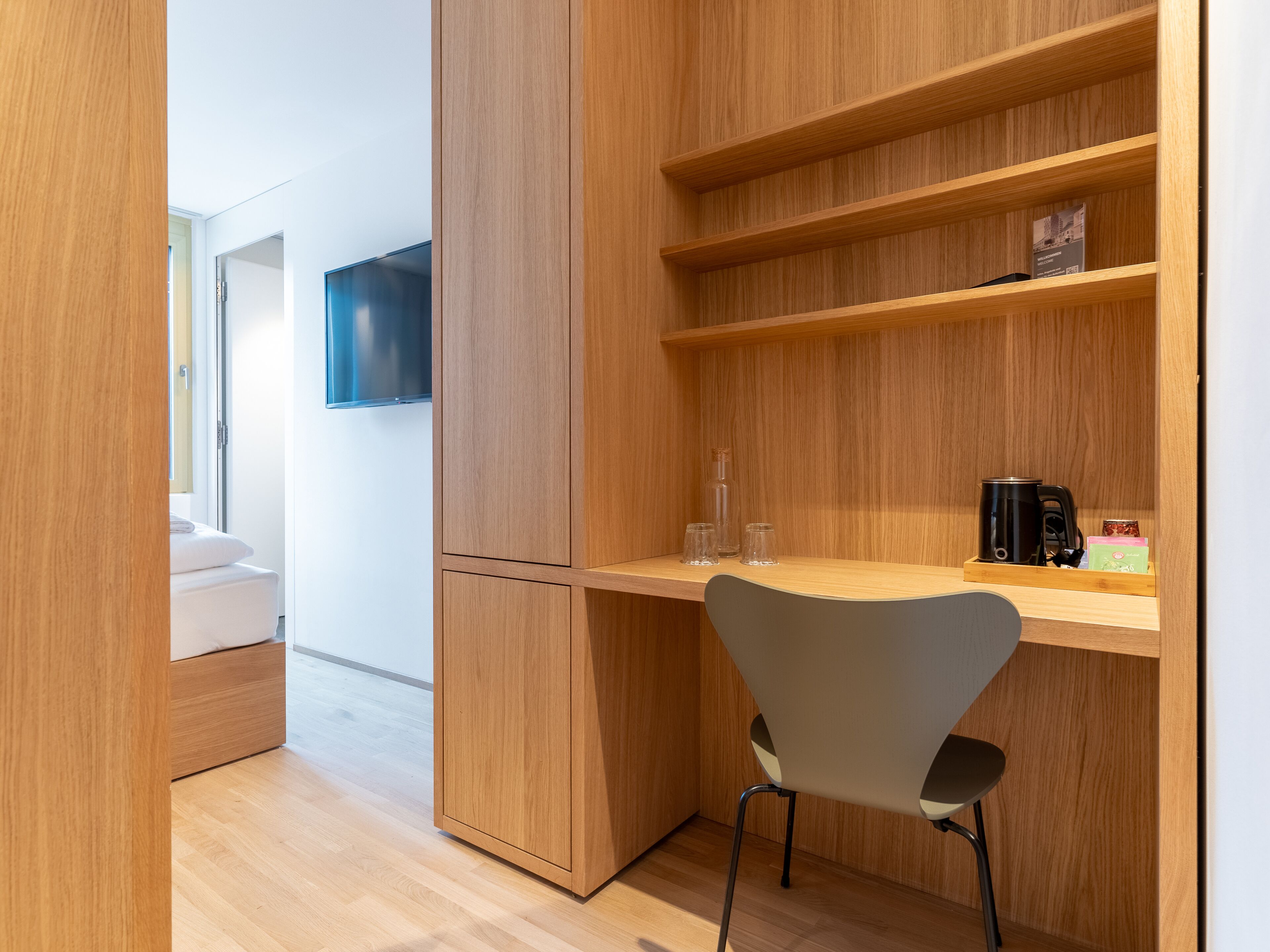 A modern room with a wooden desk, a chair, a television, and a bed.