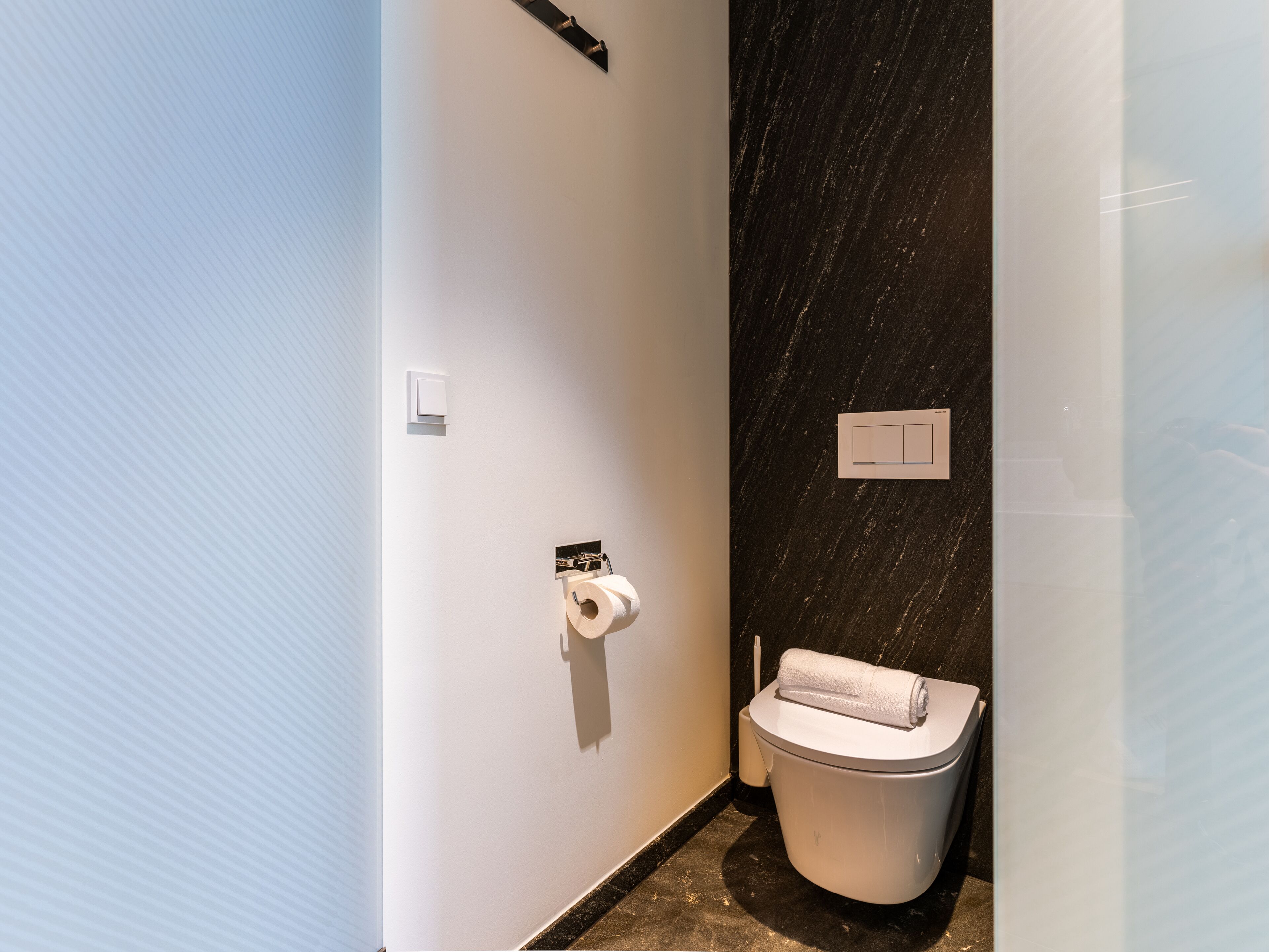 Ein kleines, modernes Badezimmer mit Toilette, Handtuch und Papierhandtuchspender.