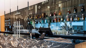 Un espace bar doté d’un comptoir en marbre, d’étagères remplies de différentes bouteilles d’alcool et d’une caisse enregistreuse.