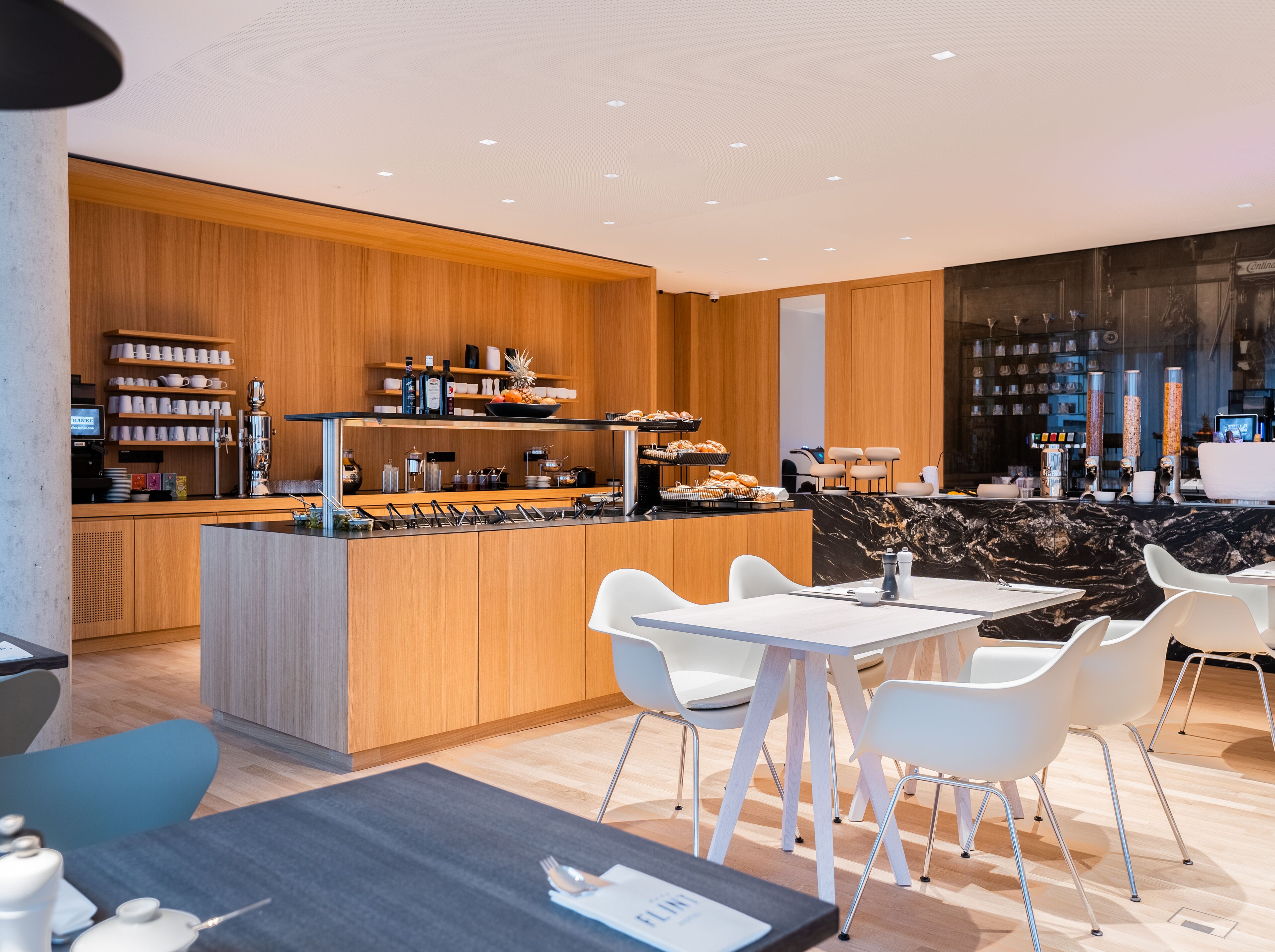A modern cafe with a wooden counter, white chairs, and a marble backsplash.