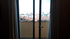 Vista a través de una puerta corrediza de vidrio hacia un balcón exterior con un paisaje urbano de fondo.