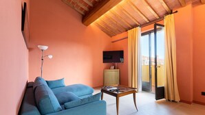 Una sala de estar con un sofá azul, una mesa de centro de vidrio, un televisor y un ventanal corredizo que da a un balcón exterior.