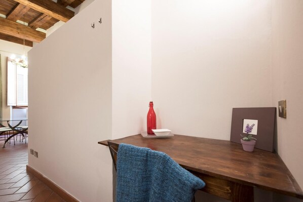 A small, cozy room with a wooden desk, a red bottle, a white bowl, and a framed picture on the wall.