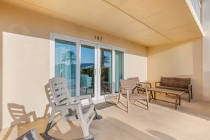 A covered outdoor seating area with a sliding glass door, numbered 102, and a view of palm trees and mountains.