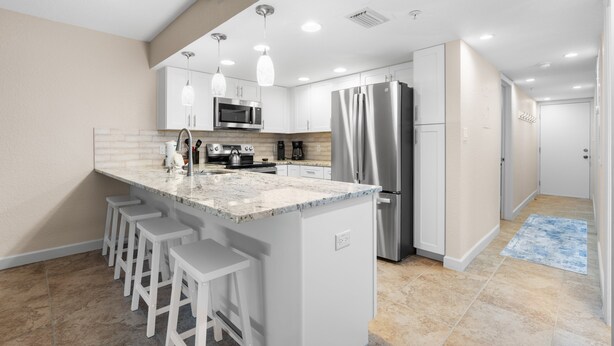 A modern kitchen with white cabinetry, stainless steel appliances, and bar stools. - Updated Condo with Intracoastal Views & Direct Vehicle Access – Indian Rocks Beach Retreat (Indian Rocks Beach)